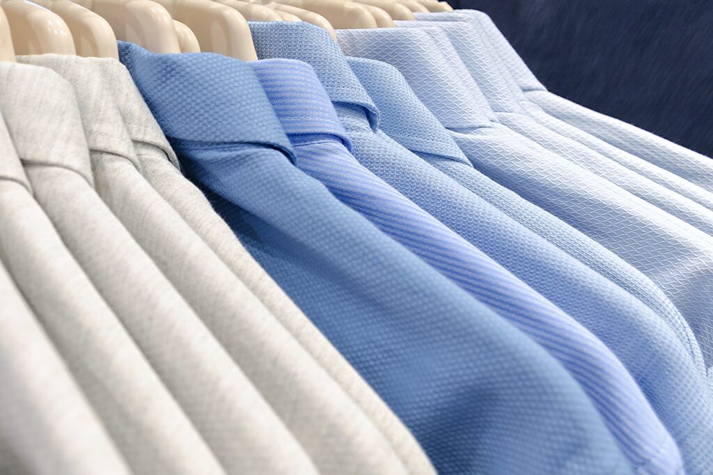 Classic men's shirts made of cotton light cool tones on the clothes hanger in the store. Selling wear in blue color. Photo with shallow depth of field.